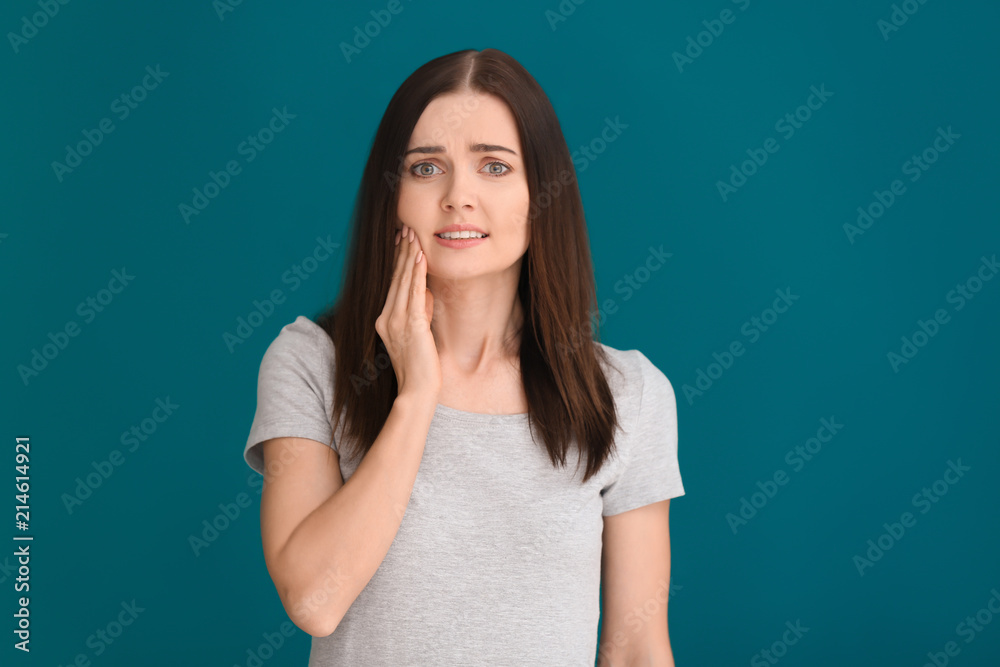 Young woman suffering from toothache on color background
