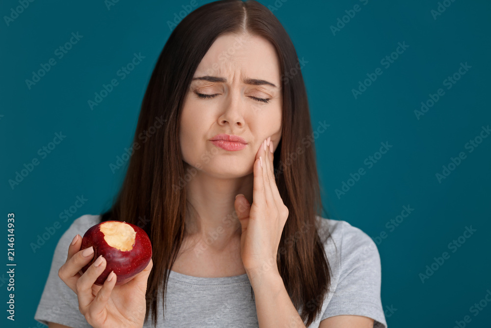 Young woman with sensitive teeth and apple on color background Young woman with sensitive teeth and apple on color background