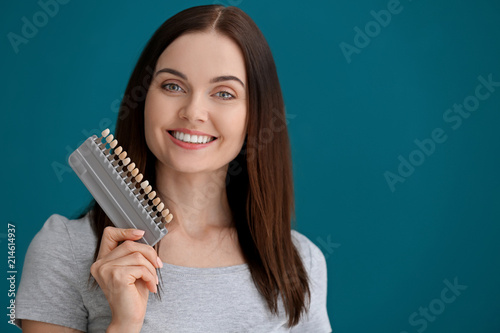 Beautiful young woman with teeth samples on color background
