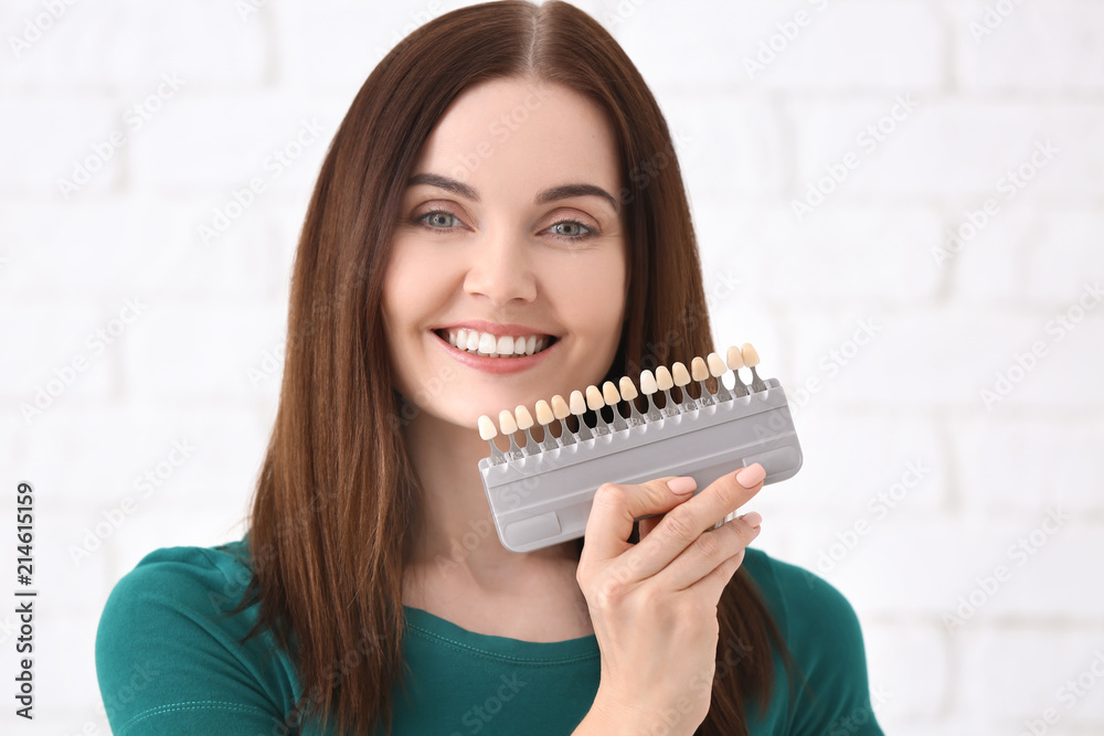 Beautiful young woman with teeth color samples on blurred background Beautiful young woman with teeth color samples on blurred background