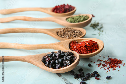 Spoons with different dry spices on color background