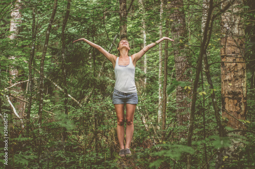 A young woman with arms outstretched in the forest enjoys nature