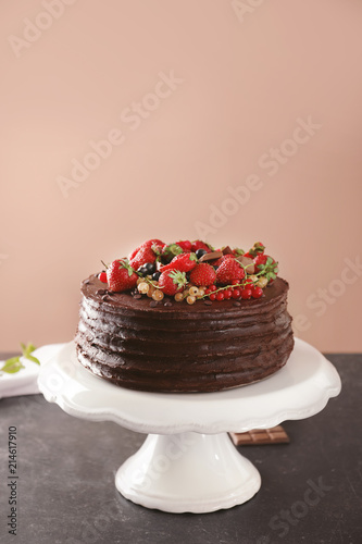 Tasty chocolate cake with strawberries and currants on table against color background