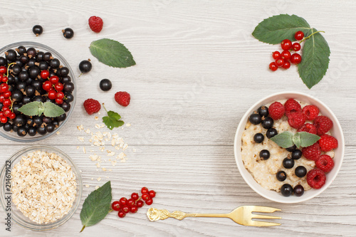 Oatmeal porridge in porcelain bowl with currant berries and raspberries, decorated with mint leaves