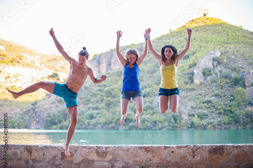 Friends jumping on a embankment on a turquoise lake in the mountains 