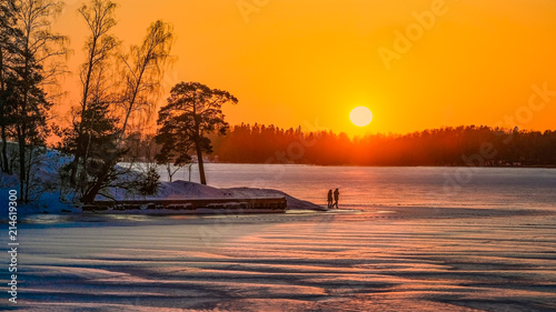  A winter landscape at sunset from Lapland. A couple walks over a frozen lake