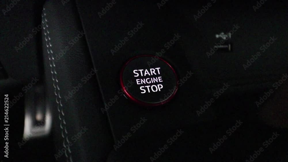 Finger pushing start engine button very dark close up. The button is backlit.