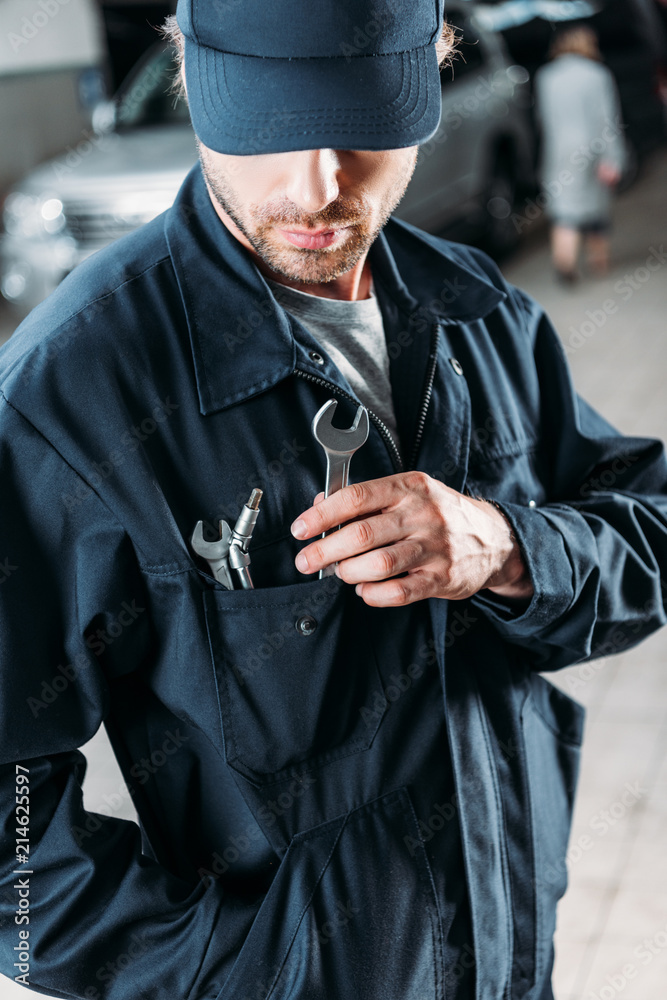 workman in cap and overalls holding tools in pocket