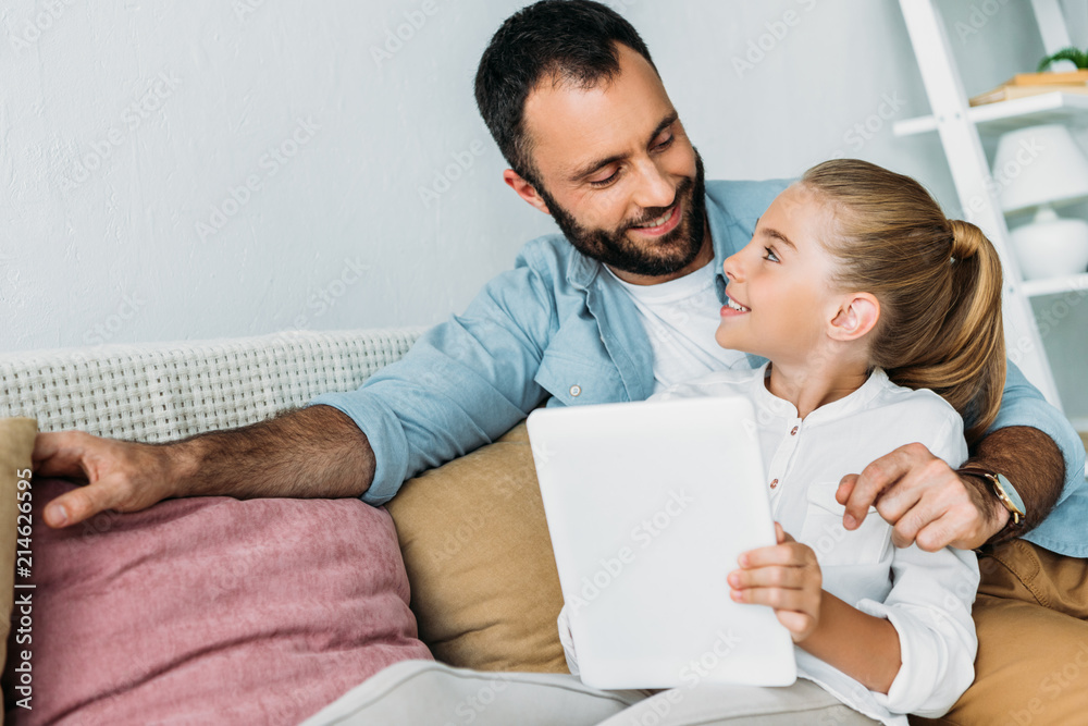 father and daughter using tablet together while sitting on couch at home father and daughter using tablet together while sitting on couch at home