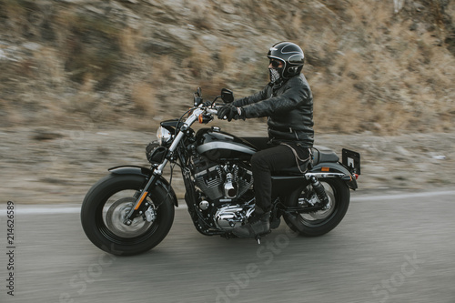 Fototapeta Naklejka Na Ścianę i Meble -  Man in black clothes riding a black classic American motorcycle in a road.