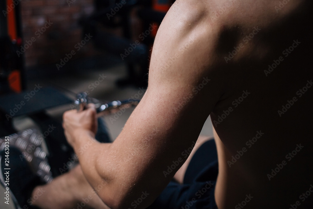 Closeup of a handsome power athletic man bodybuilder doing exercises with dumbbell. Handsome man doing biceps lifting in a gym.Dark background. Unrecognizable, no face portrait