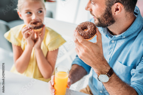 Εκτύπωση καμβά close-up shot of happy father and daughter eating doughnuts with orange juice at