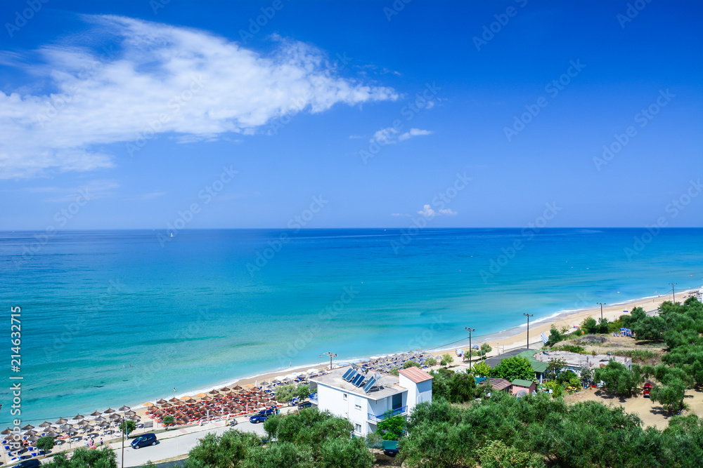 View from the terrace on a long sandy beach with yellow sand and turquoise blue sea in the afternoon. Background with blue horizon.
