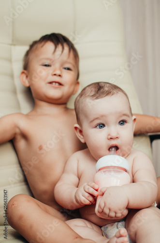 brother feeding little sister with milk or cereal with a bottle photo