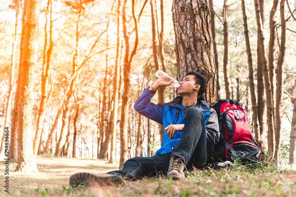 Young traveler Man with backpack drinking water at nature forest during traveling on vacation, freedom lifestyle outdoor concept with sunlight
