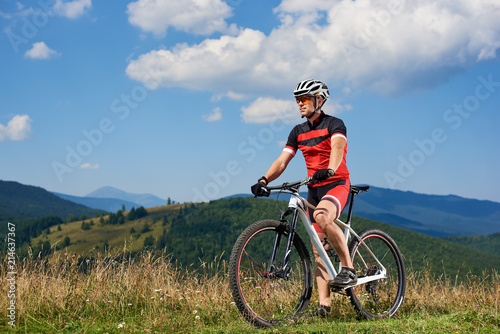 Young athletic professional cyclist in sportswear and helmet cycling mountain bicycle. Male rider enjoying beautiful mountains on sunny summer day. Active healthy lifestyle and extreme sport concept