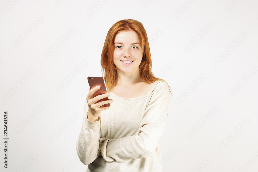 Young attractive natural redhead woman smiling at smartphone screen, using mobile phone, wearing loose white shirt. White background, copy space. Beautiful female using online dating app concept. Young attractive natural redhead woman smiling at smartphone screen, using mobile phone, wearing loose white shirt. White background, copy space. Beautiful female using online dating app concept.