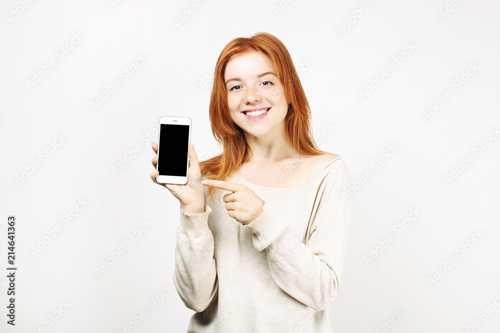 Young beautiful natural red head woman smiling wide with perfect smile, showing blank screen of smartphone. Attractive female pointing at mobile cellphone display w/ index finger Copy space background Young beautiful natural red head woman smiling wide with perfect smile, showing blank screen of smartphone. Attractive female pointing at mobile cellphone display w/ index finger Copy space background