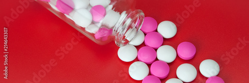 Pink and white pills scattered from a glass jar.
