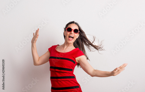 A young beautiful delighted woman with red sunglasses and t-shirt in a studio.