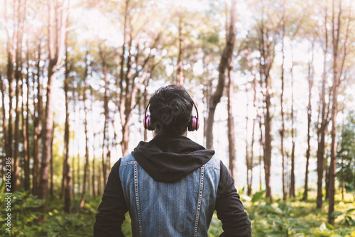 Man listening to music on the headphones standing in the forest with sunlight