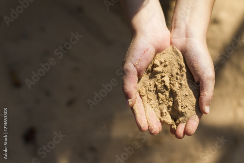 Child's hands holding a handful of sand on sunny day