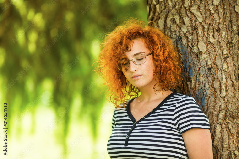 Young woman with ginger hair leaning on a tree