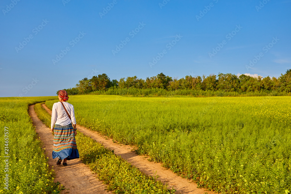 A young woman walks on the road through a flowering meadow