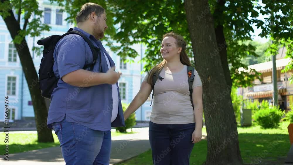 Young overweight man and woman holding hands and nuzzling in park, students love Young overweight man and woman holding hands and nuzzling in park, students love