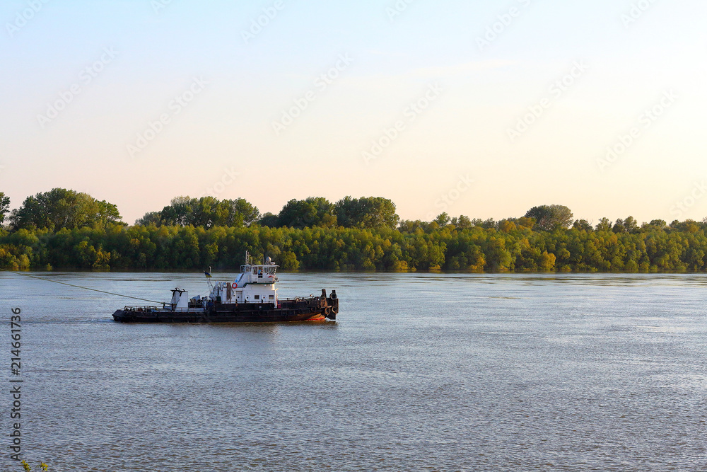 Small tugboat moves along the riverbank of Danube river