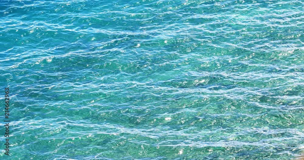 Crystal clear and transparent water surface texture of turquoise sea waves in tropics. Shiny ripples reflect sunlight at sunny day. Tranquil and serene meditative background