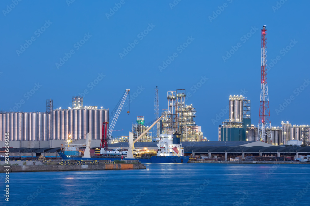 Wharf of petrochemical production plant with moored vessel against a blue sky at twilight, Port of Antwerp, Belgium.