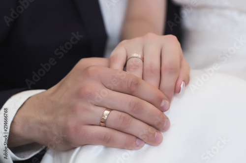 Groom holds bride's hand in white dress with rings on wedding day.