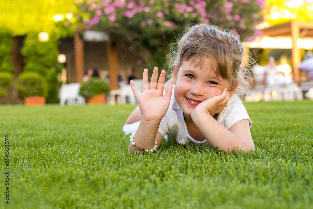 Adorable smiling girl laying in the grass and waved her hand Adorable smiling girl laying in the grass and waved her hand