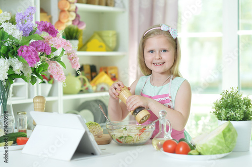 Cute little girl spicing salad on kitchen table