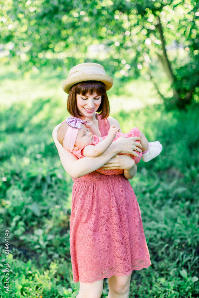 Beautiful Mother with the straw hat And her little daughter outdoors family look in in a pink dress . Outdoor Portrait of happy family. family look. Mother and baby in park portrait