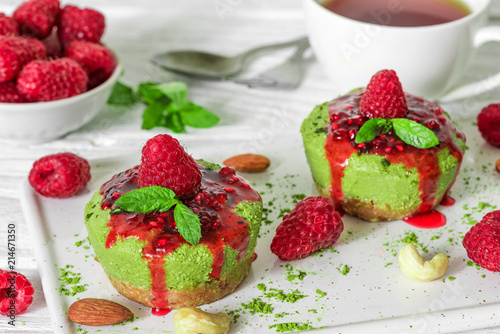 Fototapeta Naklejka Na Ścianę i Meble -  green matcha and banana vegan raw cheesecakes with raspberries, mint, nuts and coffee cup topped with jam