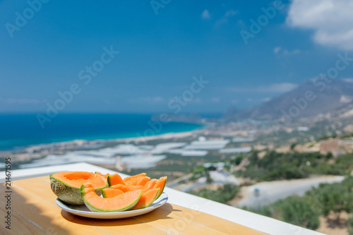 Yellow melon on a plate on a table with view on sea and mountain. Falassarna, Crete, Greece