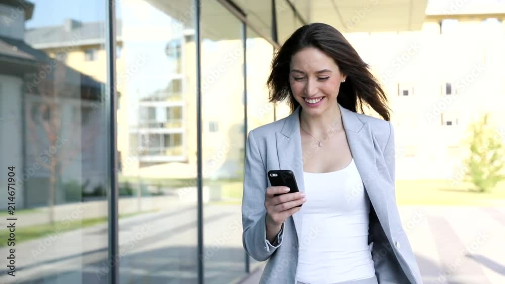 Young Successful Businesswoman Walking in the City. Chatting on her Mobile Device. Surfing the Internet. Stylish Outfit. Woman with Charming Smile. Slow Motion. Business Lifestyle. Young Successful Businesswoman Walking in the City. Chatting on her Mobile Device. Surfing the Internet. Stylish Outfit. Woman with Charming Smile. Slow Motion. Business Lifestyle.