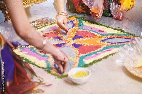 Bride's friend helps coloring the traditional rice art (Rangoli) on the floor for indian wedding © manees