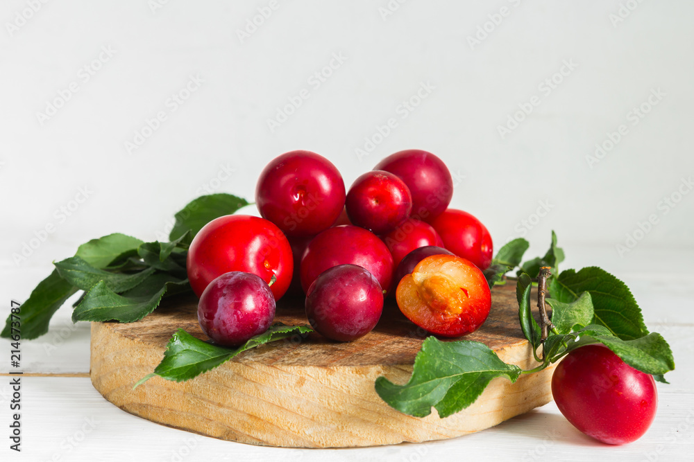 Fresh red plum with leaves on a wooden light background Fresh red plum with leaves on a wooden light background