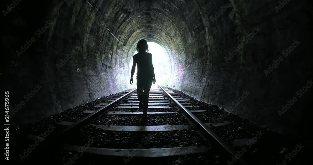 Woman entering into long dark railroad tunnel and walks inside by tracks. Conceptual psychological scene of human freedom and hope