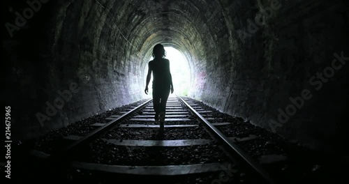 Woman entering into long dark railroad tunnel and walks inside by tracks. Conceptual psychological scene of human freedom and hope photo