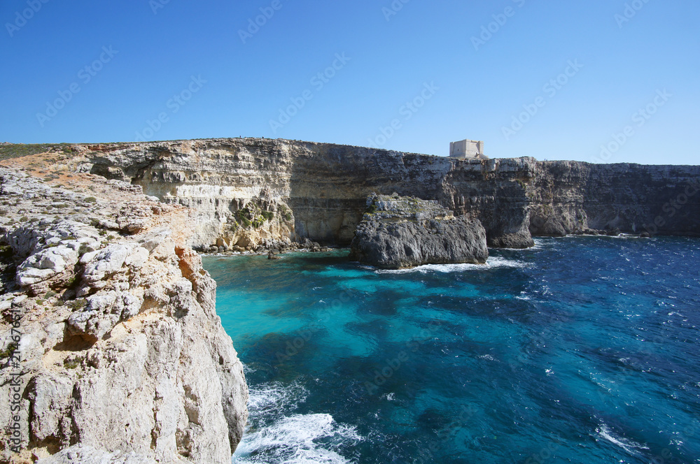Blue lagoon with high cliffs and Santa Marija Tower on Commino Island in Malta (Torri ta' Kemmuna)