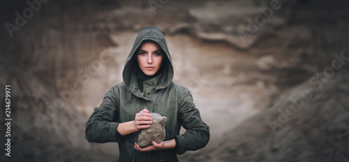 A young woman holds a stone in her hands. The concept of a biblical metaphor about collecting stones. Atone for sins. Cataclysm, destruction, ruins. photo