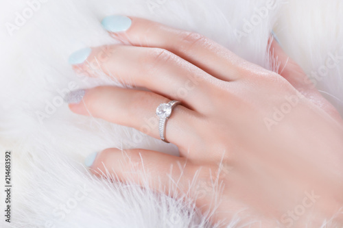 Diamond engagement wedding ring on female finger and hand on fur white background. Jewelry and beauty concept. Close up  selective focus