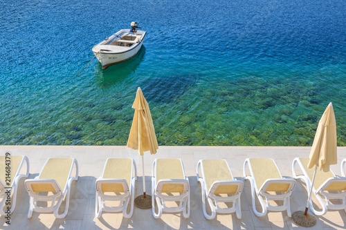 Boat in the turquoise Adriatic sea with the chairs and umbrellas on the pier © erikzunec