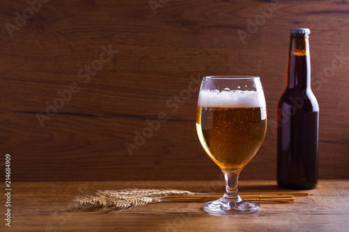 Glass and bottle of beer, ears of barley on wooden table. Ale. Room for text