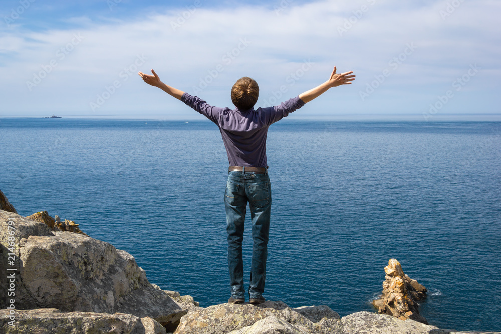 A man looks at the sea with his hands spread wide on a sunny spr A man looks at the sea with his hands spread wide on a sunny spr