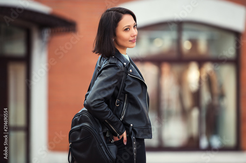 Young fashion woman in black leather jacket walking in city street